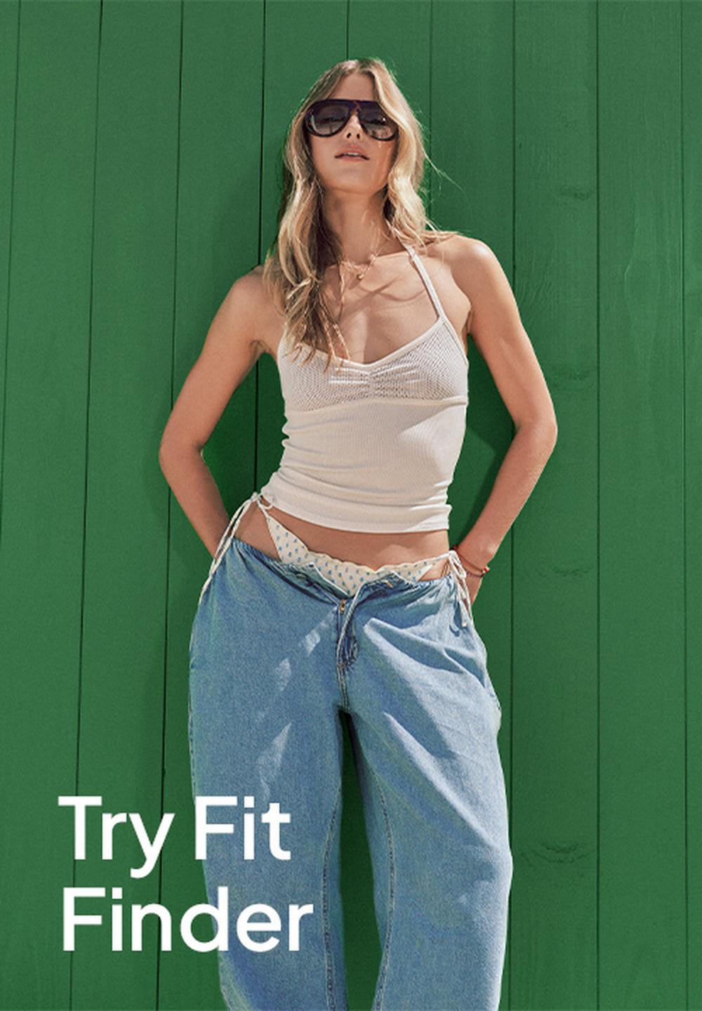 Promotional fashion image of a woman in sunglasses and a white tank top with loose blue jeans standing against a bright green wall, with the text “Try Fit Finder” in the lower left corner.