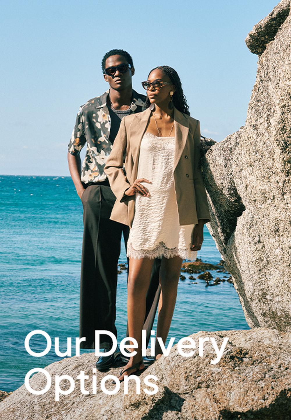 Promotional Superbalist banner with a stylish man and woman standing on seaside rocks in sunglasses and fashionable clothing, overlaid with the white text “Our Delivery Options.”