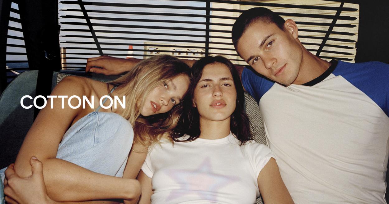 Cotton On fashion campaign with three young models lounging together in casual basics, including white and blue tops, with the COTTON ON logo on the left
