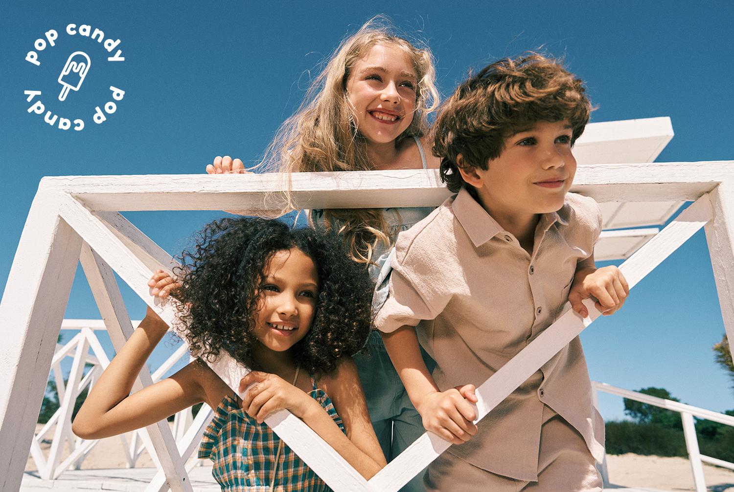 Kids in colorful summer clothes walking down a beach ramp, with a girl in front holding a bright green Pop Candy flag.