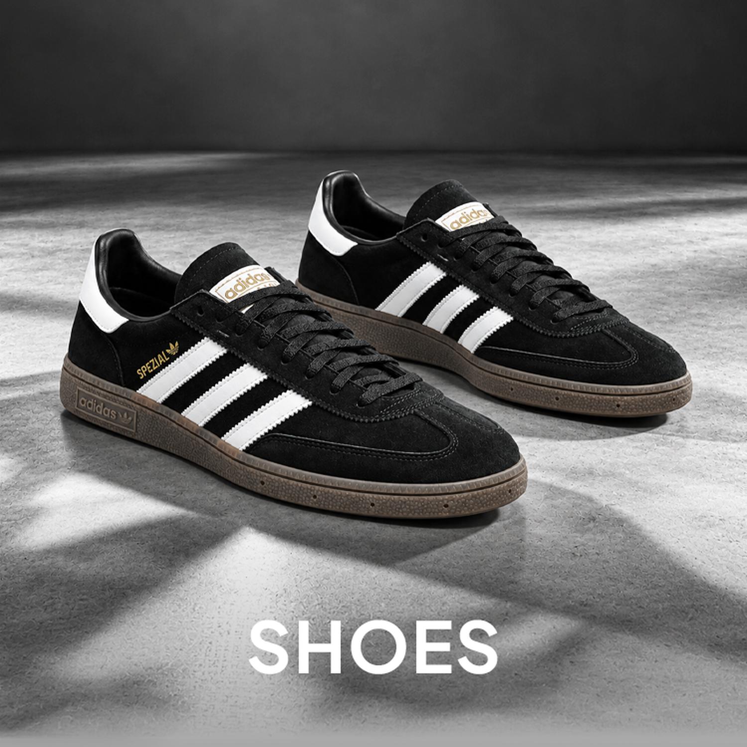 Black-and-white promo image of a pair of black Adidas sneakers on a gray floor, with the word “SHOES” centered at the bottom.