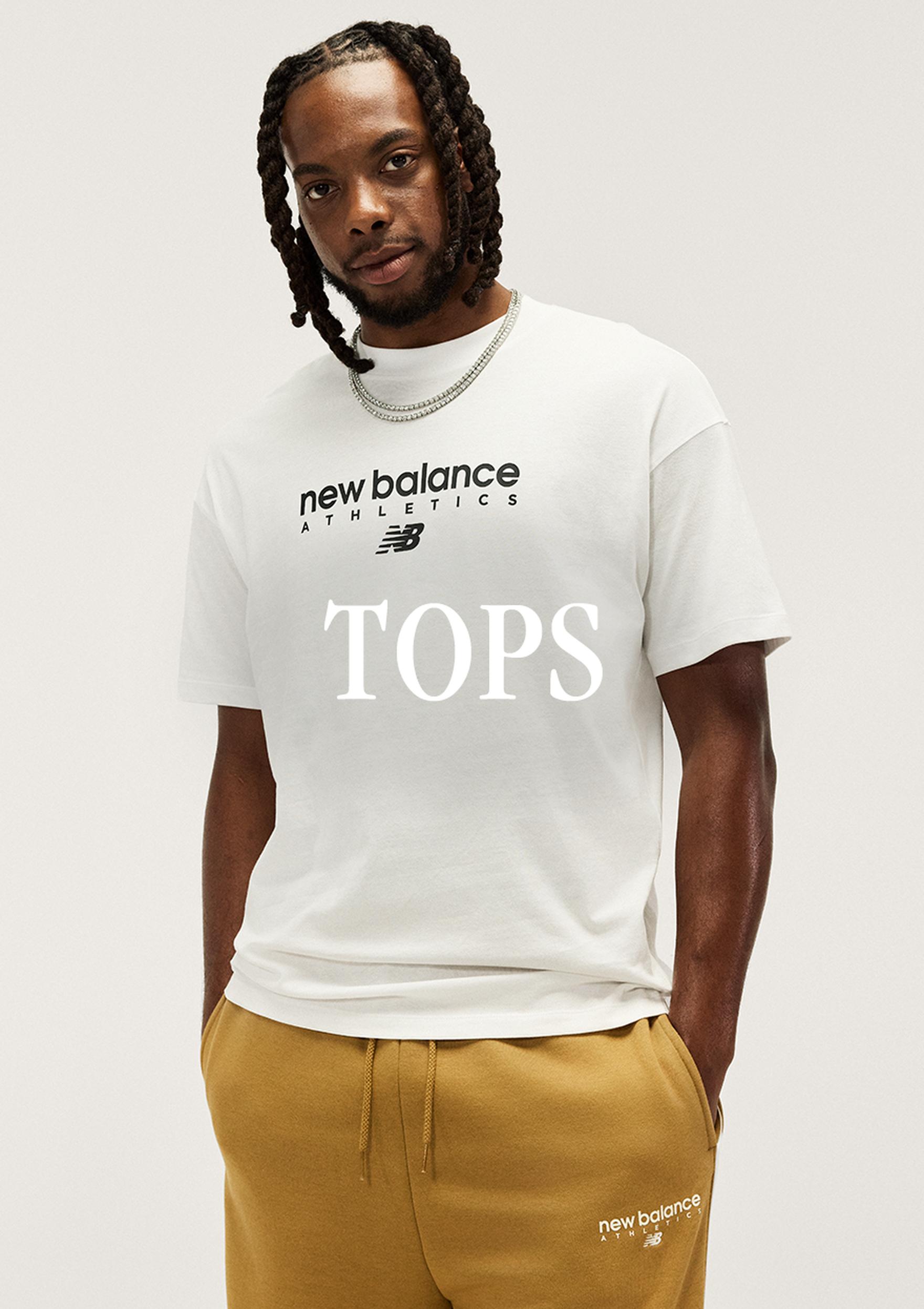 A male model in a white New Balance Athletics T-shirt and mustard joggers stands against a plain studio background, with “TOPS” overlaid across the shirt.