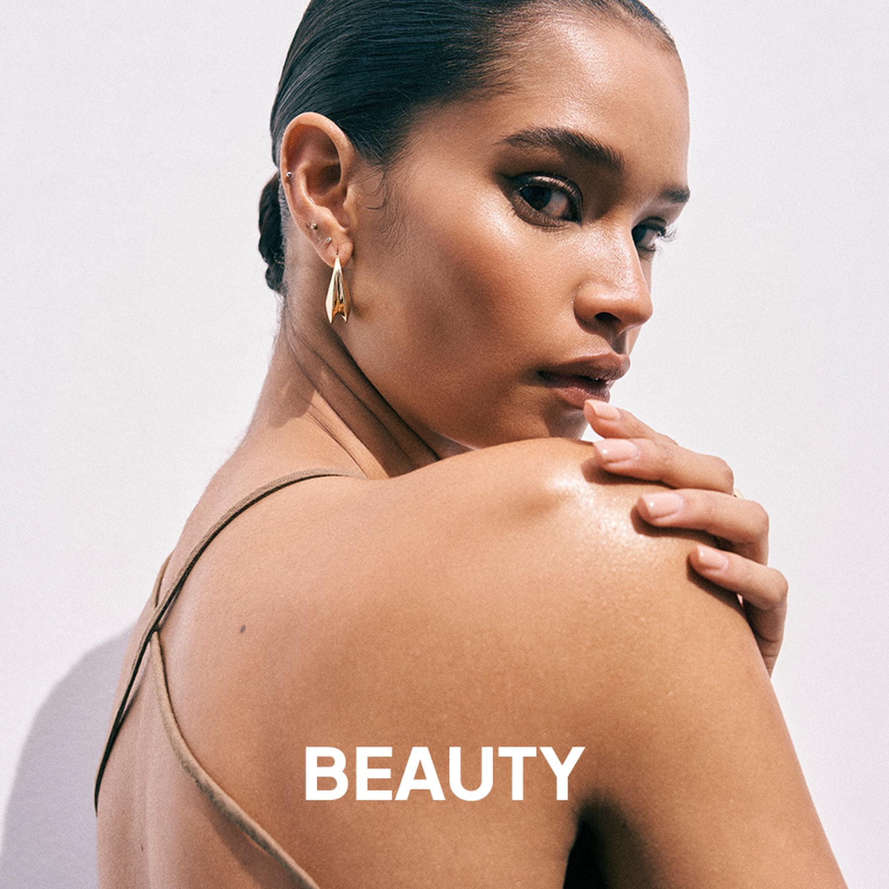 A model wearing a deep red pleated halter neck dress and large silver statement earrings. Beauty and accessories collection.