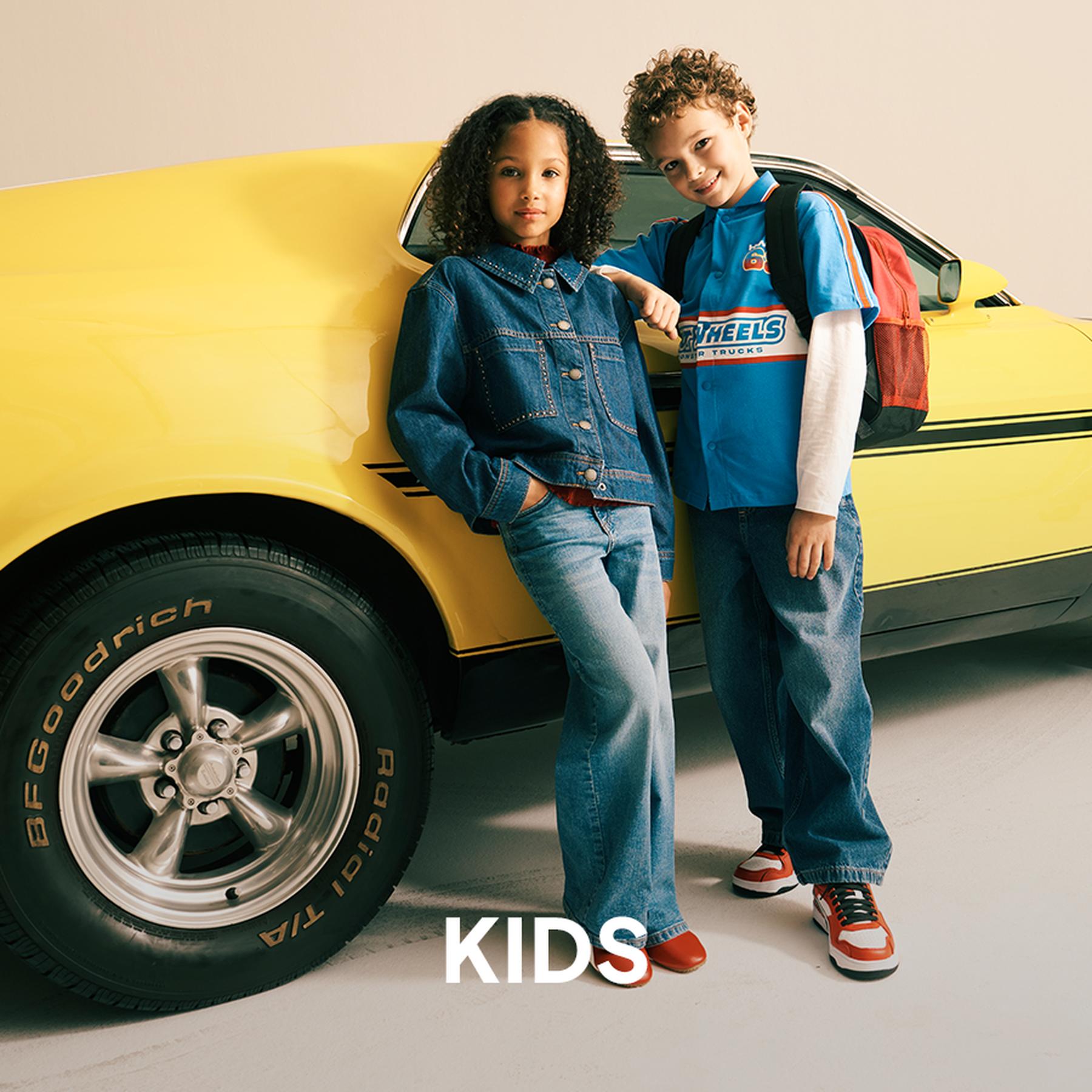 A girl in a beige puffer jacket and pink button-down skirt, and a boy in an olive green jacket and brown trousers, both wearing boots. Kids' collection.