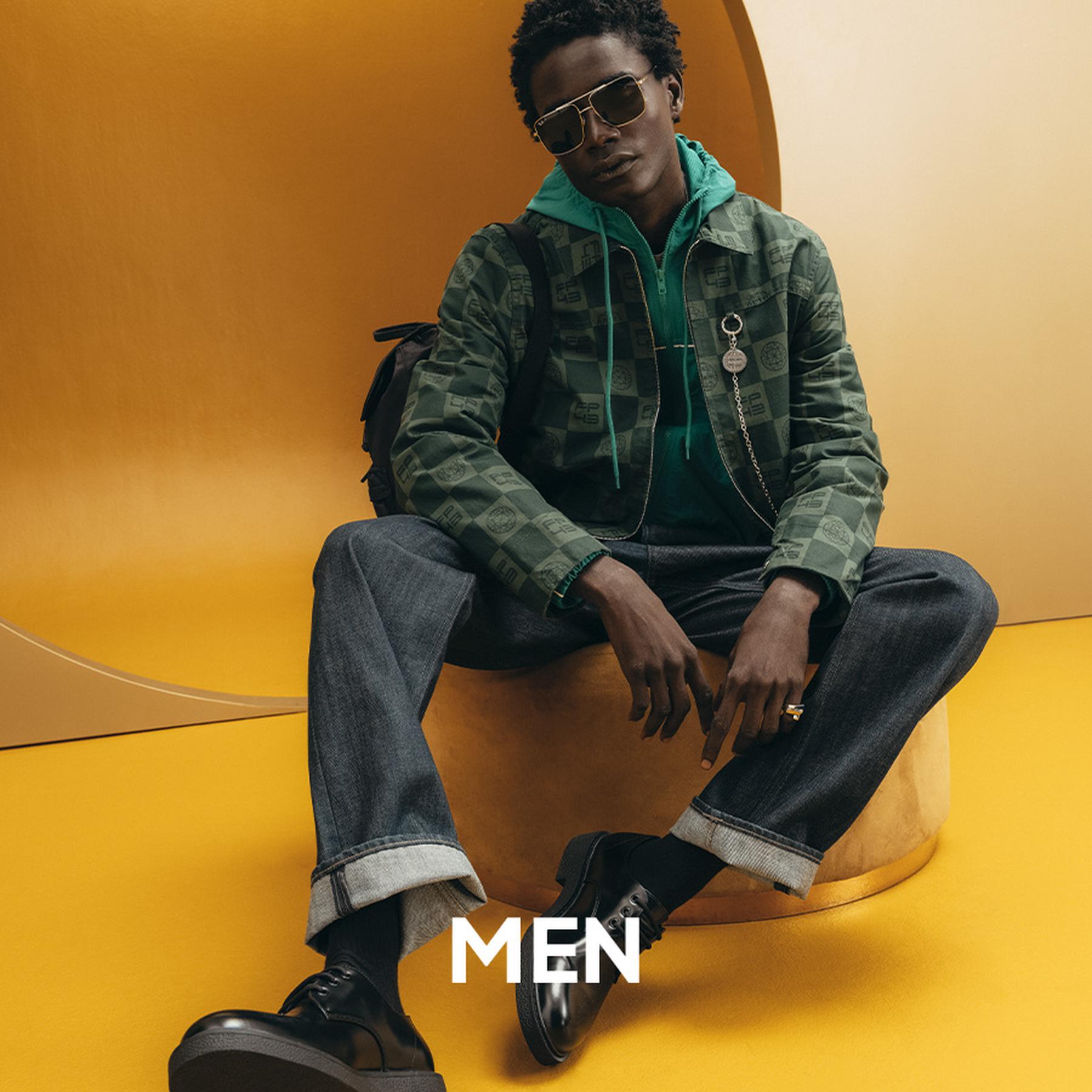 Male model in a leather biker jacket and relaxed-fit pants with sunglasses, showcasing modern men's fashion. Men's apparel.