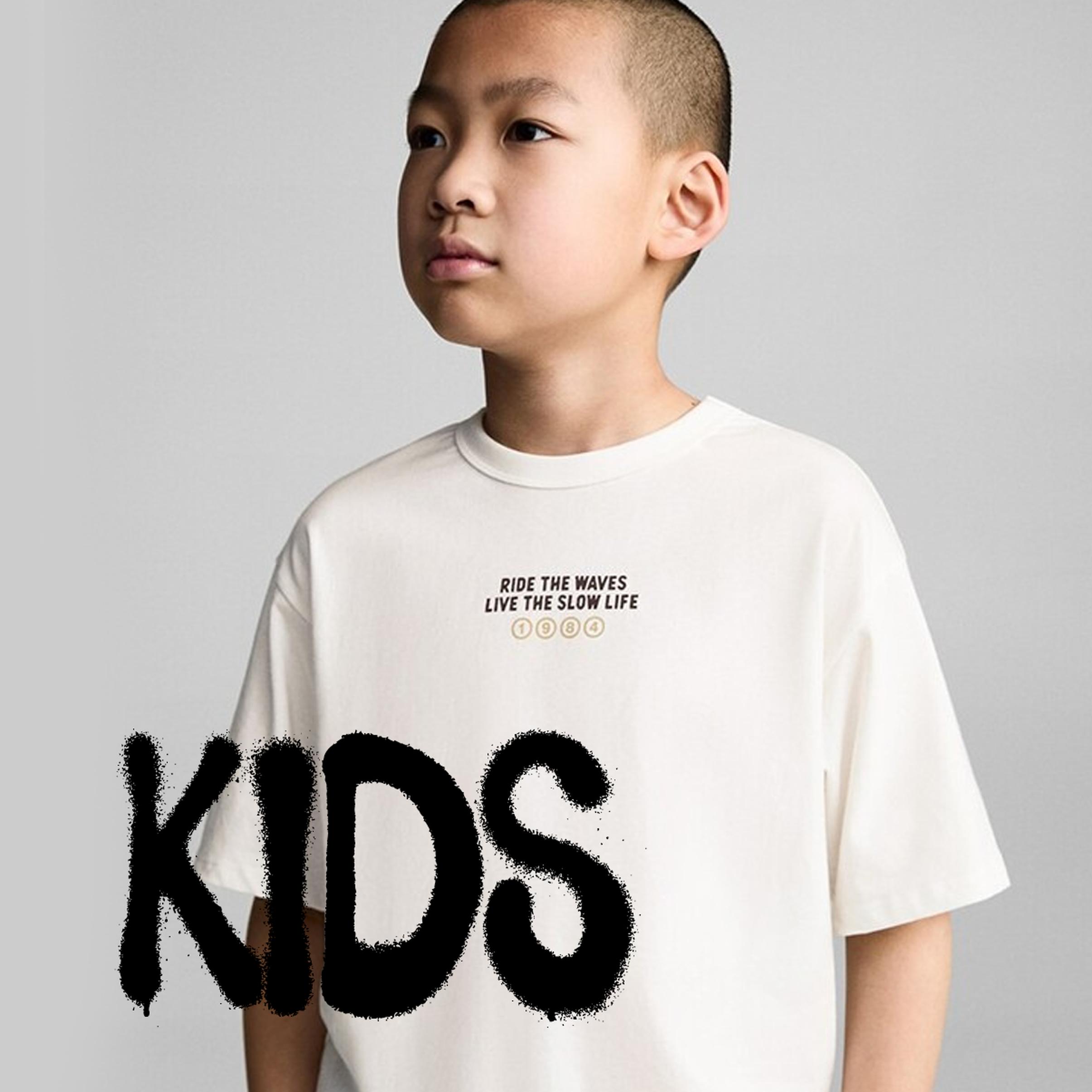 Young boy wearing an oversized white T-shirt on a light gray background, overlaid with large black “KIDS” text, matching the Black Friday kids clothing deals section.
