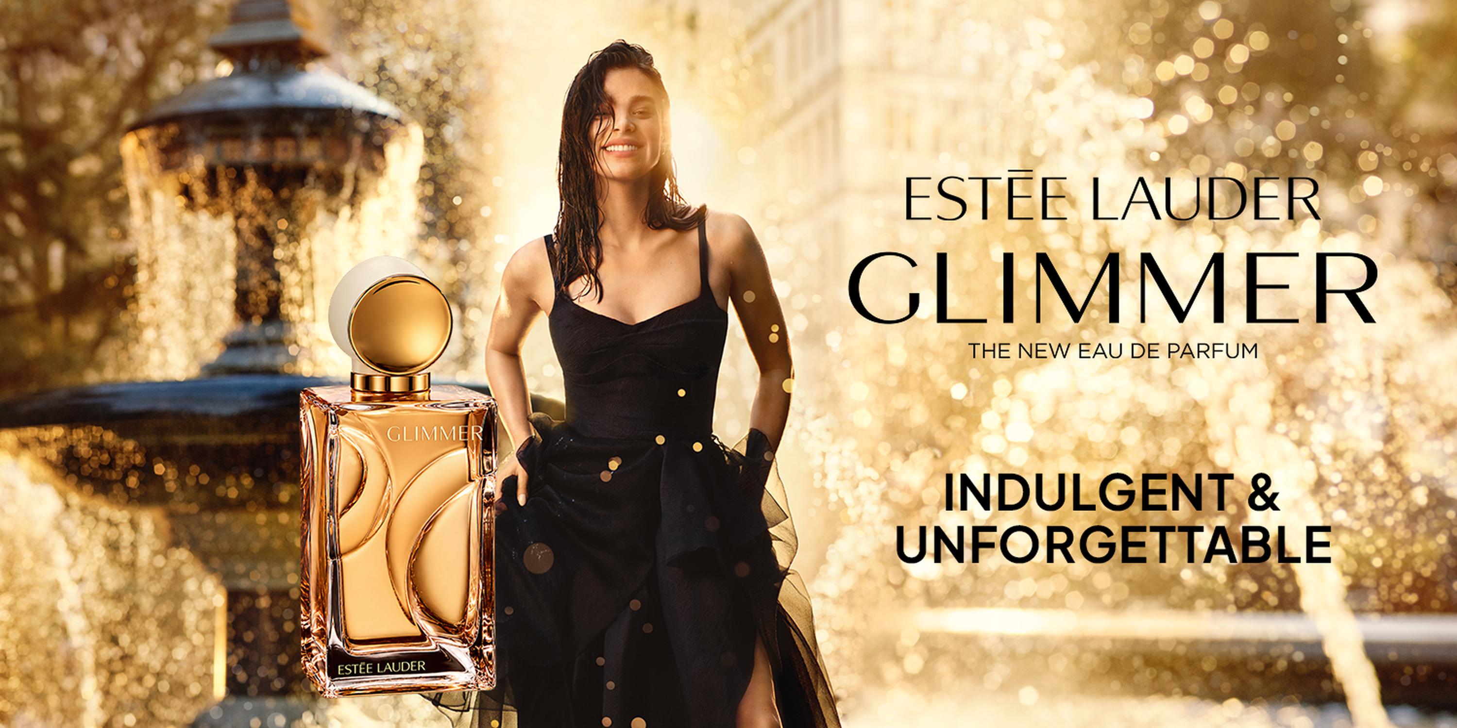 Estée Lauder Glimmer perfume ad with a woman in a black dress beside a gold fragrance bottle against a sparkling golden background, featuring the text “INDULGENT & UNFORGETTABLE.”