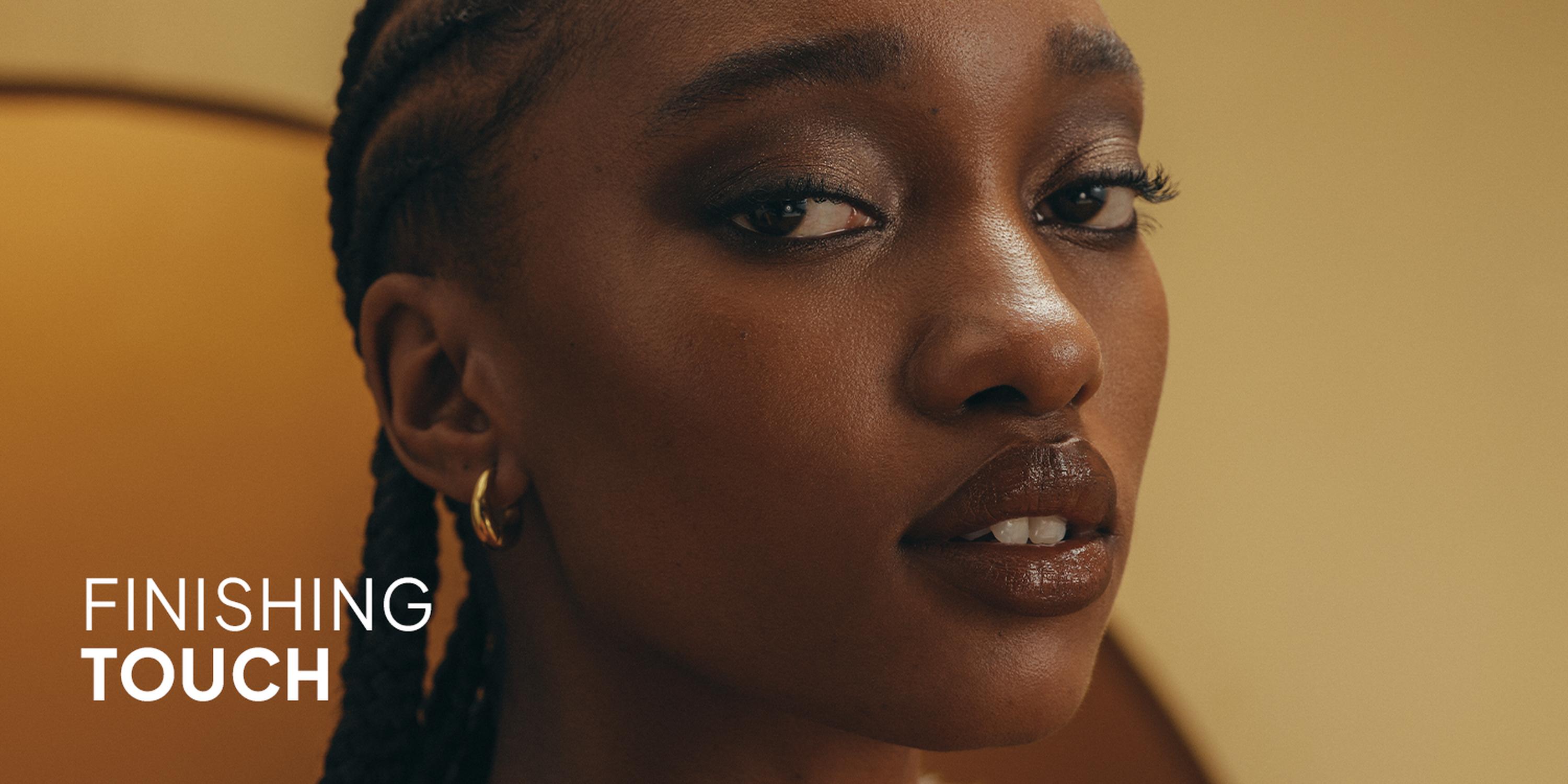 Warm Tones beauty banner featuring a model with bronzed makeup, terracotta lips, and large gold statement earrings.