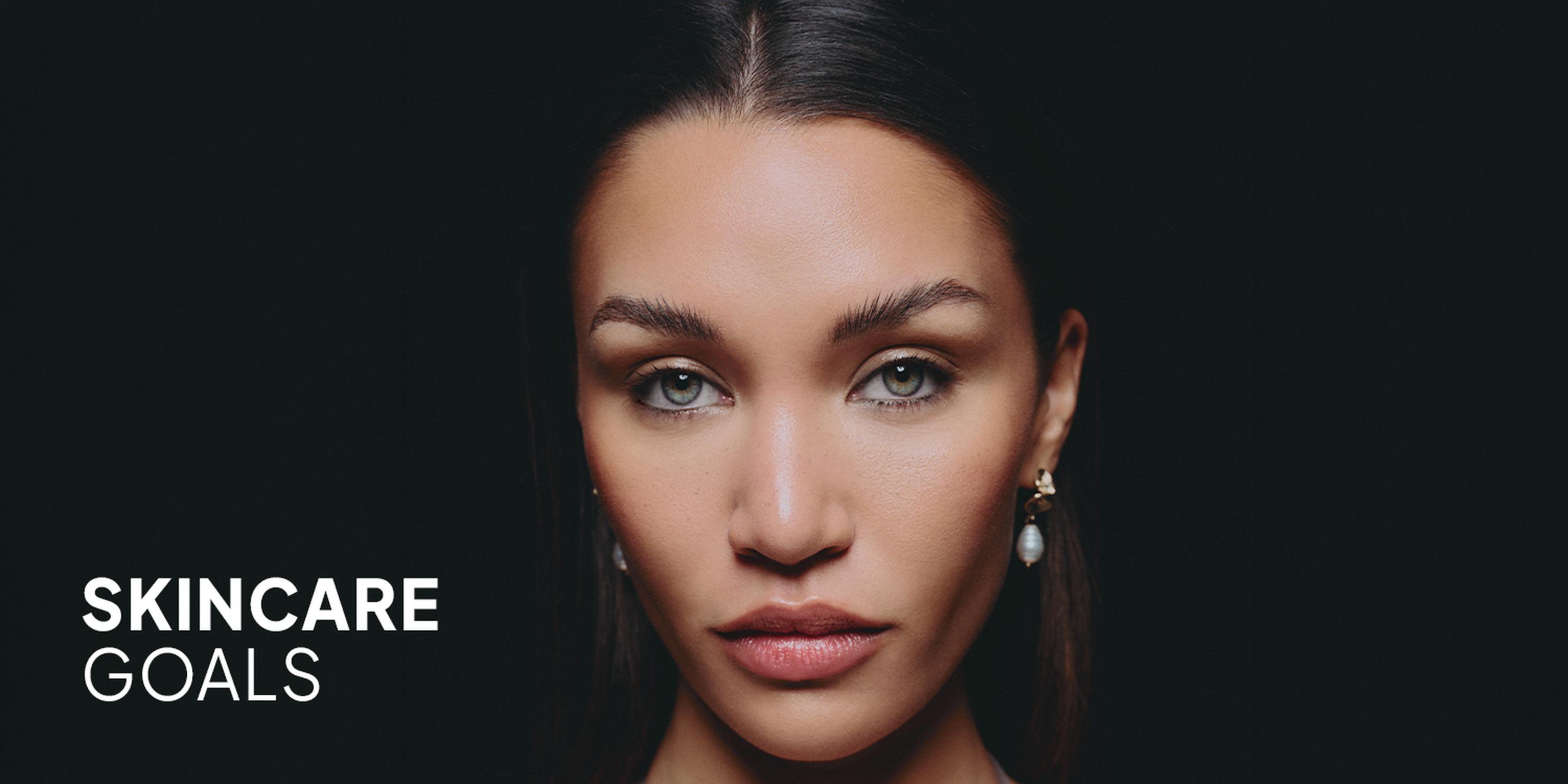 Close-up beauty ad of a woman with a flawless face on a dark background, with the text “SKINCARE GOALS” beside her.