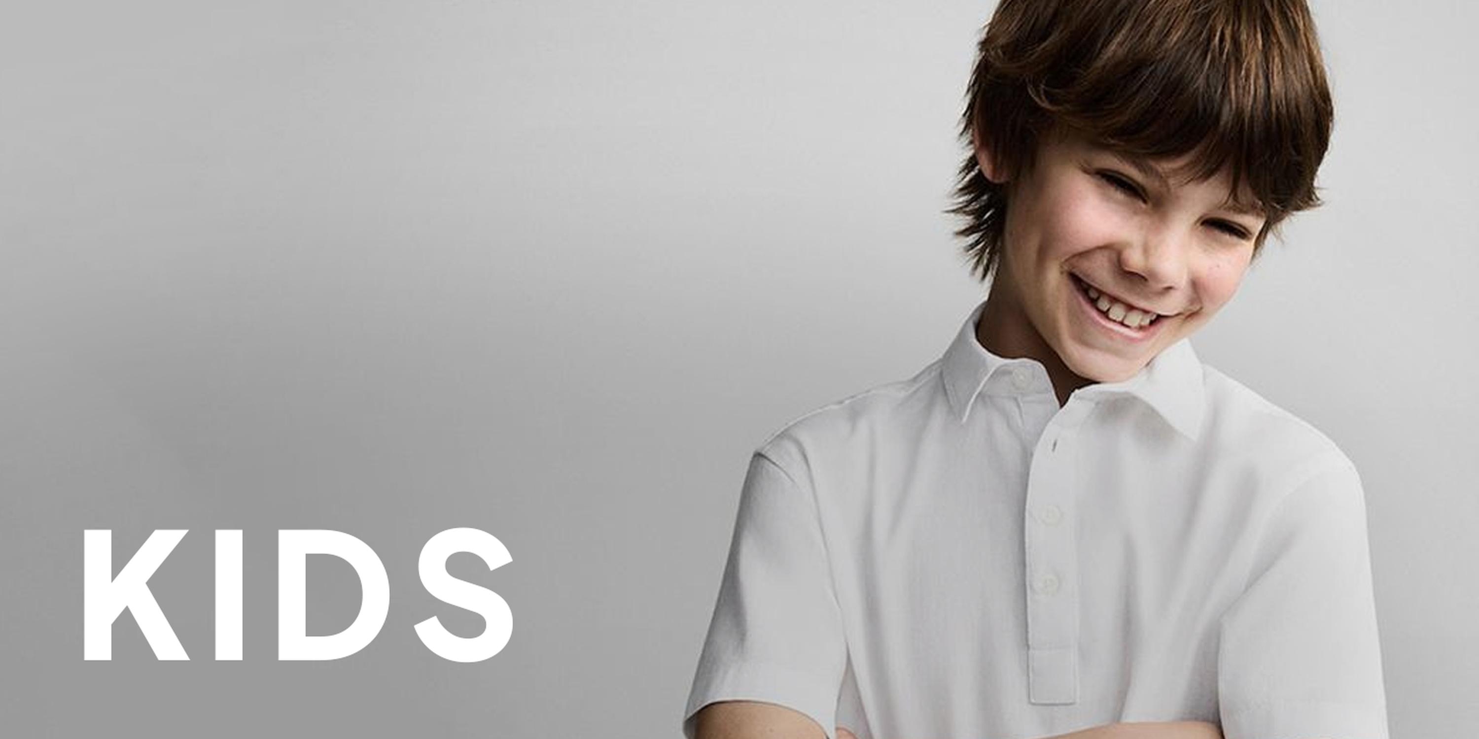 Young boy wearing an oversized white T-shirt on a light gray background, overlaid with large black “KIDS” text, matching the Black Friday kids clothing deals section.