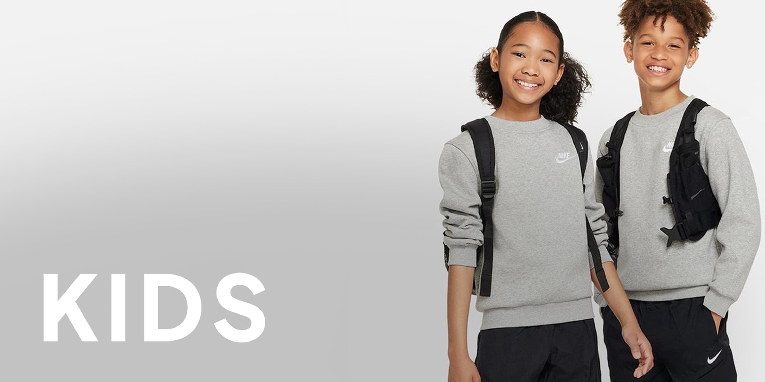Black Friday Nike kids banner on a light gray background, with two smiling children wearing gray sweatshirts and black backpacks next to large “KIDS” text.