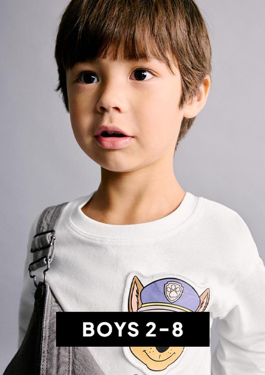 Young child in a light blue T-shirt and pink shorts on a white background, with a blue paint-stroke label reading “BOYS 2–8” for Cyber Monday kids’ deals.