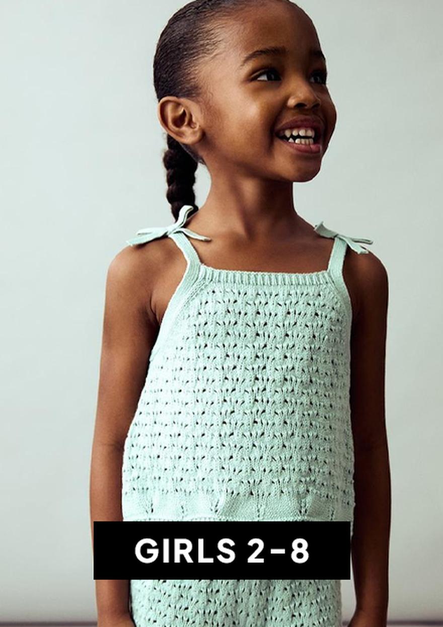 A young girl wearing a white dress with sheer puff sleeves and star details on a white background, labeled “GIRLS 2–8” for the Black Friday kids clothing deals section.