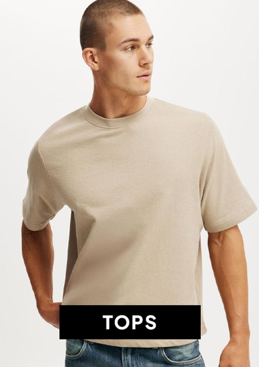 Close-up of a man wearing a cream sleeveless knitted top, with a black “TOPS” label, shown as part of Black Friday men’s clothing deals.