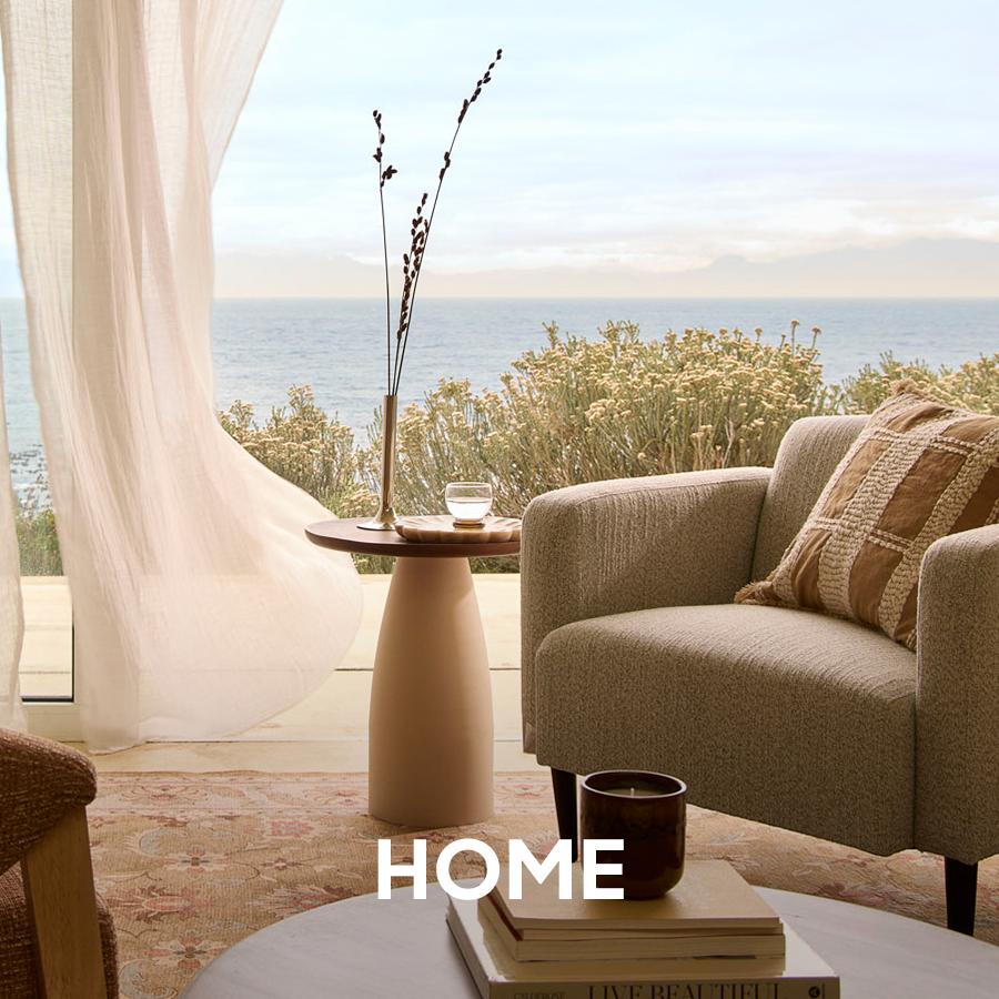 Modern white outdoor armchairs and sculptural side tables are arranged on a dark wood deck. Home and patio collection.