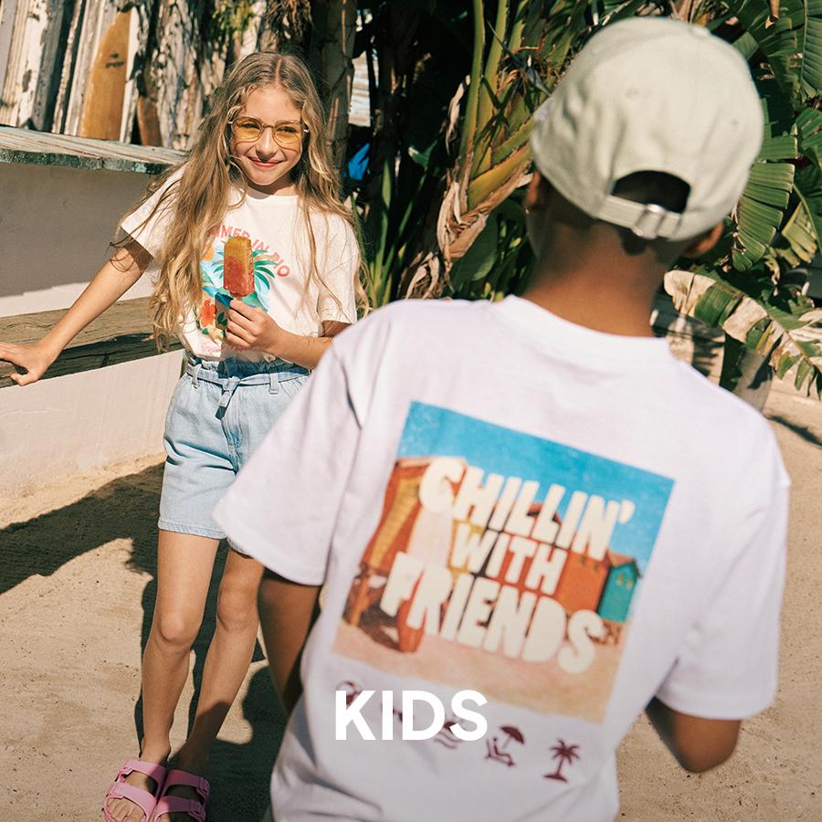 Two smiling children outdoors in summer clothes holding popsicles, with “KIDS” text overlaid.