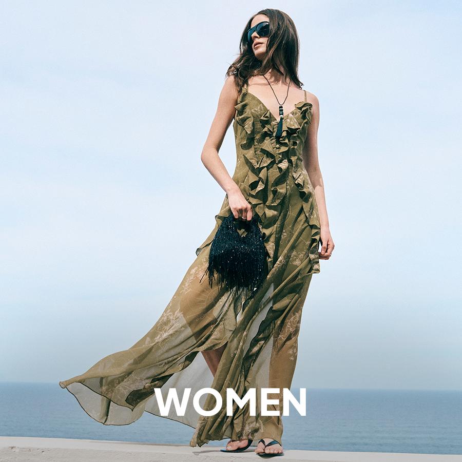 A woman in an oversized dark chocolate brown coat holding a matching suede clutch bag in a minimalist studio. Women's collection.